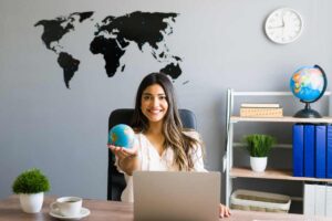 Mujer sosteniendo el mundo en las manos mostrando el globo sonriendo mientras trabaja en su moderna oficina